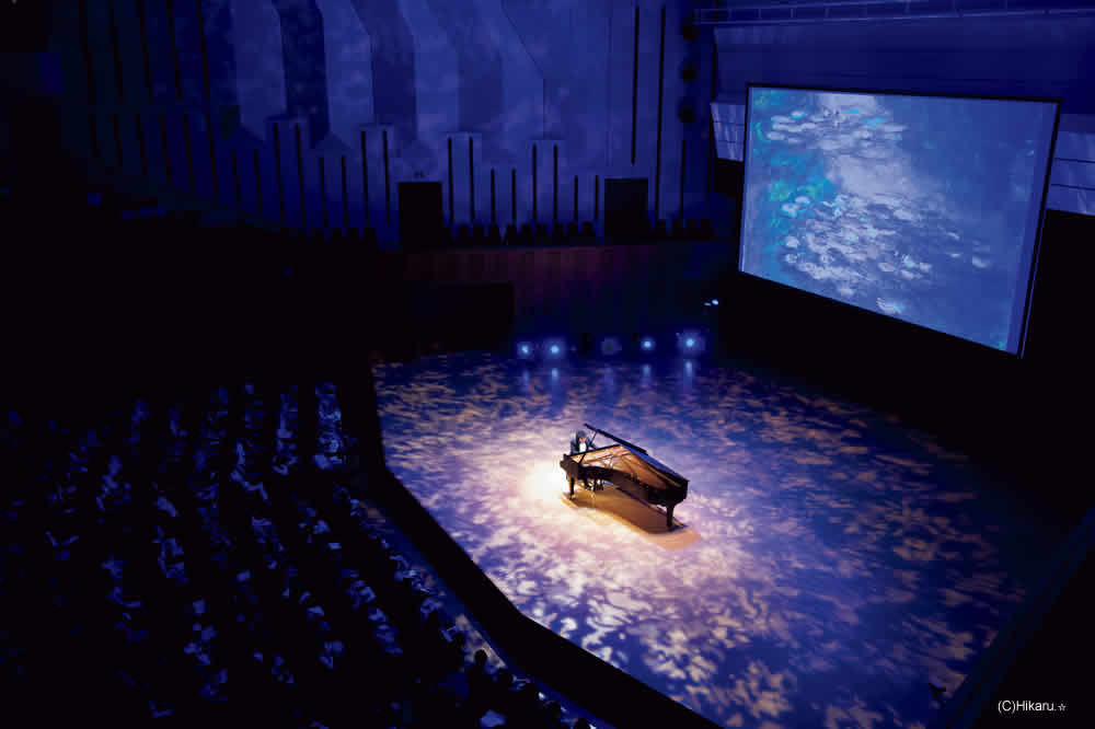 辻井伸行　音楽と絵画コンサート　≪印象派≫　会場イメージ写真　　ドビュッシー、サティ、ラヴェルなどの印象派を代表する名曲を生演奏でお届けするとともに、ステージ上の大型スクリーンにルノワール、モネをはじめとする印象派の巨匠たちの名画、さらには葛飾北斎の浮世絵やクリムト、ミュシャ、ロートレックなどの作品を高画質で投影　音楽と絵画が融合する視覚と聴覚に深い感動を与える特別なコンサート